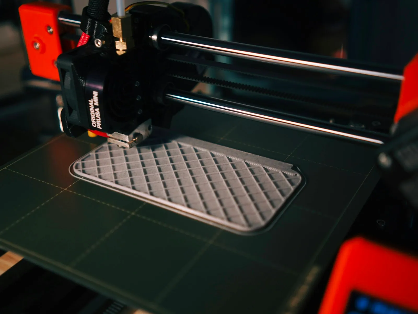 Impresora 3D fabricando una pieza técnica gris con estructura de rejilla